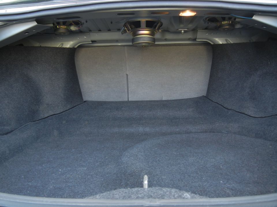 Car trunk interior with dark grey carpet, speakers mounted on the ceiling, and folded down rear seats