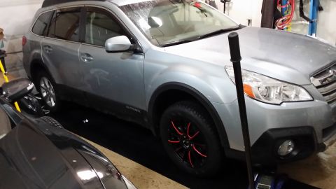 2014 Subaru Outback - A silver Subaru Outback is parked in a garage, showing its front passenger side and custom wheels.