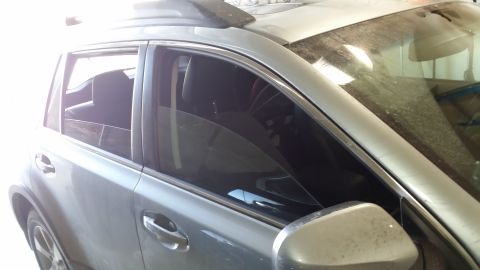 2014 Subaru Outback - This silver SUV has a dusty windshield and dark tinted windows with an aftermarket visor strip above the windows.