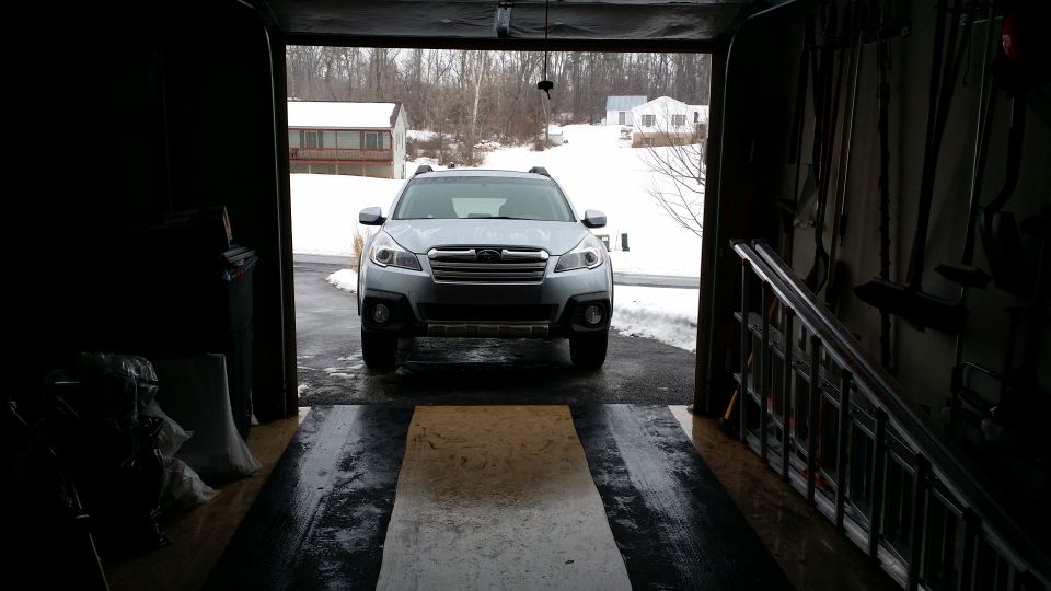 Silver 2014 Subaru Outback parked facing forward in a garage with snow outside