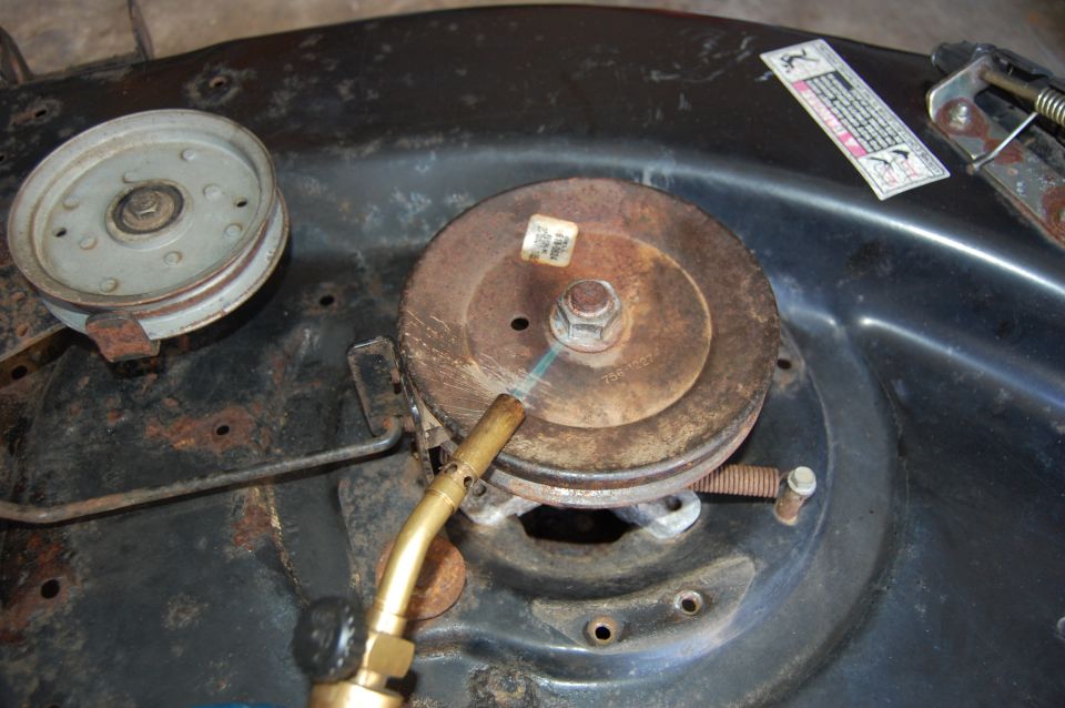 Close-up of a lawn mower deck pulley with a torch aimed at it