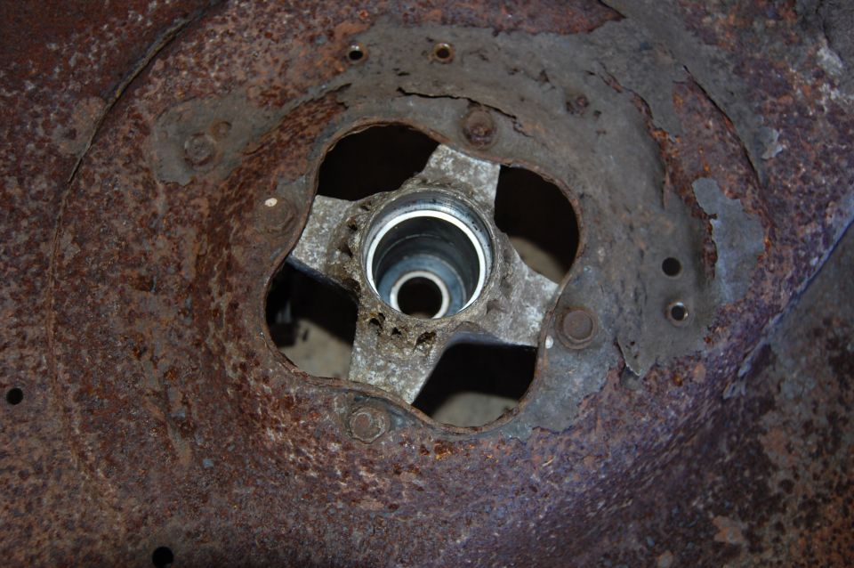 Close-up of a rusted mower deck spindle housing with a four-bolt mounting pattern