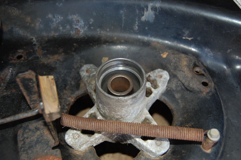 Close-up of a mower deck spindle housing with a rusty spring and metal bracket