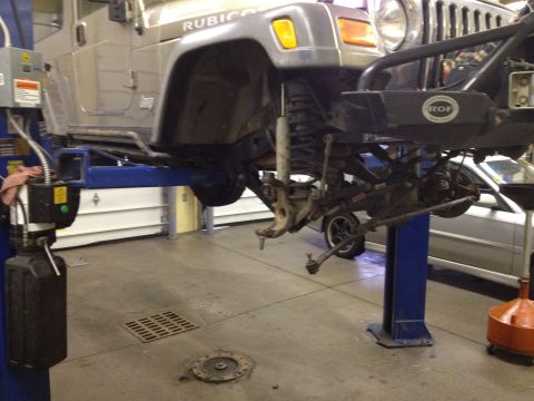 2005 Jeep Wrangler - Front suspension of a 2005 Jeep Wrangler being serviced on a lift, with 'Rubicon' badging visible on the fender.