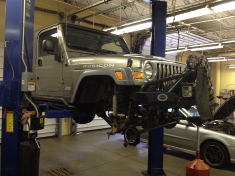 2005 Jeep Wrangler - A silver 2005 Jeep Wrangler Rubicon is shown on a lift in a garage, with its front suspension components removed for service.