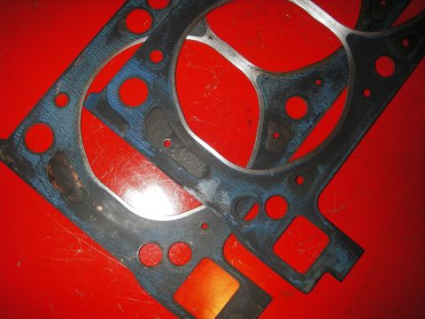 1972 Ford Ranchero - Close-up of two engine gaskets laid out on a red surface. The Supermotors.net logo is visible in the lower right corner.