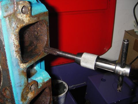 1972 Ford Ranchero - A tap tool is used to thread a rusty engine component, likely a cylinder head, in this close-up view.