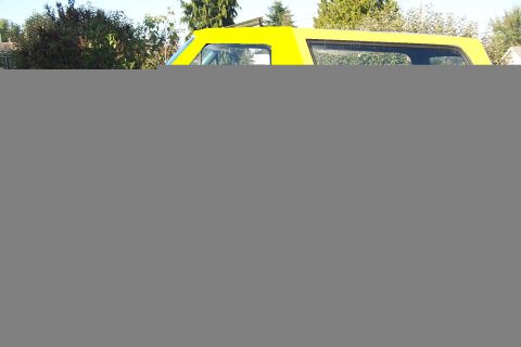 1980 Ford Bronco - Partially rendered outdoor photo showing only the upper portion of an SUV: a bright yellow removable hardtop with side and rear glass over…