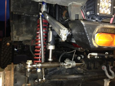 1987 Suzuki Samurai - Close-up view of modified off-road vehicle steering and suspension components, including coilovers and a turn signal.