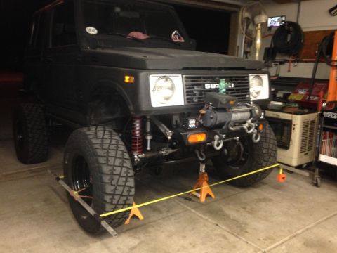 1987 Suzuki Samurai - A black 1987 Suzuki Samurai is shown on jack stands, undergoing some work in a garage.
