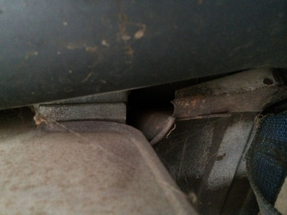 Close-up of a rusted metal bracket and a fuel tank strap, possibly from under a vehicle