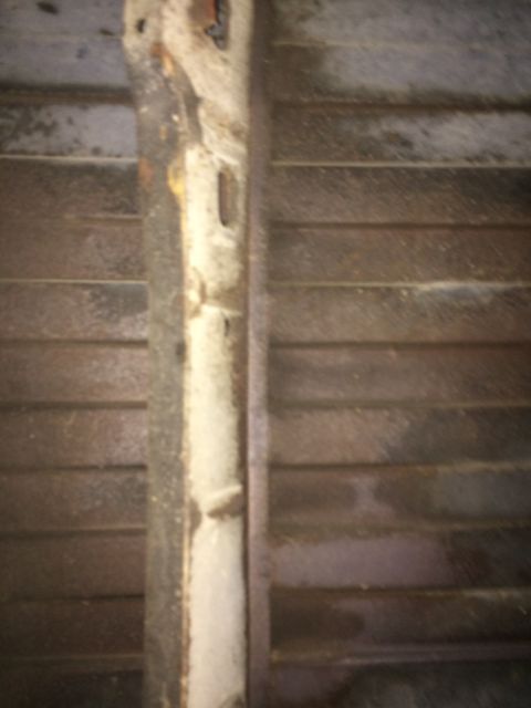 1964 Ford Ranchero - Close-up view of a rusted metal frame against a ribbed surface, possibly part of a vehicle's undercarriage.