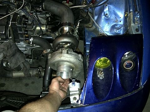 1995 Ford Probe - Close-up of a car's engine bay showing a turbocharger installation with various hoses and a hand working on a component.