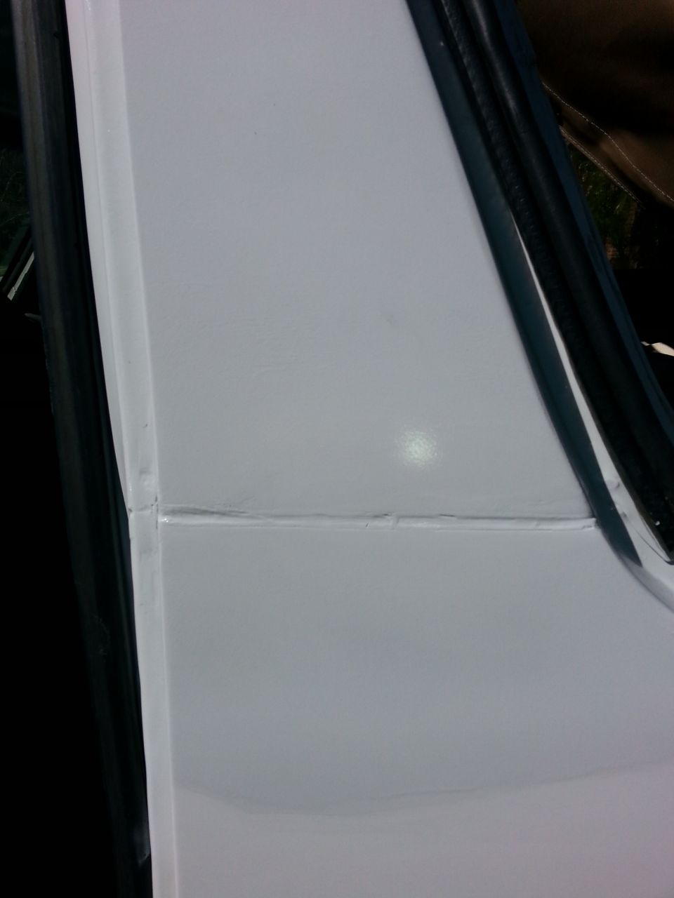 White vehicle door seam with visible repair work and a black rubber seal