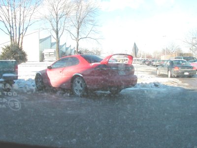 1997 Ford Taurus - A red coupe with a spoiler sits in the snow next to a pickup truck, with other vehicles in the background.
