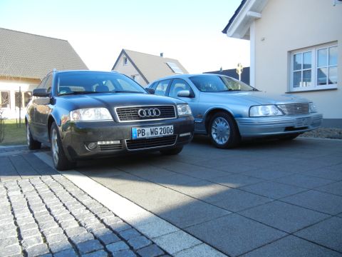 1999 Ford Fairlane - Two cars, an Audi and a light blue sedan, are parked on a paved driveway in front of a house.