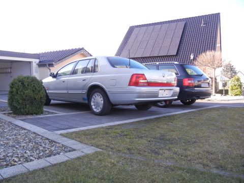 1999 Ford Fairlane - Two vehicles are parked in a driveway in front of a house with solar panels on the roof.