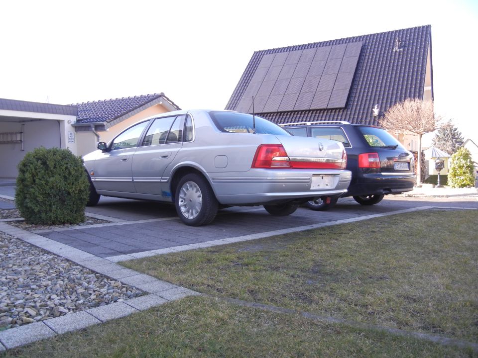 silver sedan parked next to a dark SUV in a driveway, house with solar panels in background