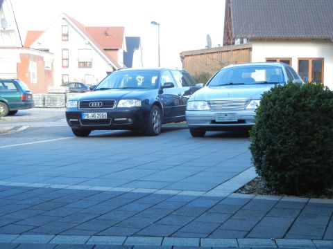 1999 Ford Fairlane - A silver sedan is parked in a driveway next to a dark blue Audi wagon.