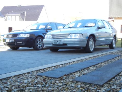 1999 Ford Fairlane - Two sedans parked on a driveway, one silver and one black.