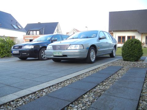 1999 Ford Fairlane - Two sedans are parked in a driveway in front of houses.