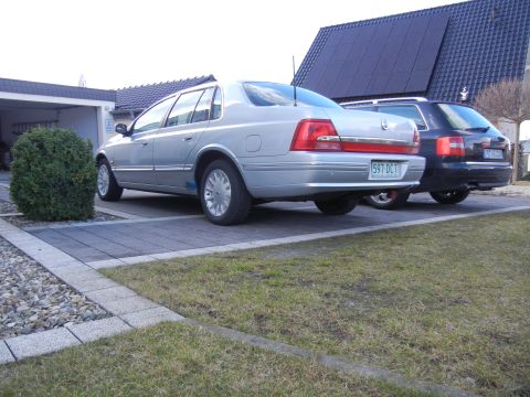 1999 Ford Fairlane - This silver sedan, possibly a 1999 Ford Fairlane, is parked in a driveway next to a dark SUV.
