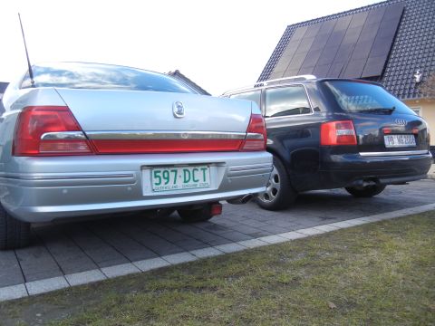 1999 Ford Fairlane - Two cars parked side-by-side in a driveway, one silver sedan and one black Audi wagon.