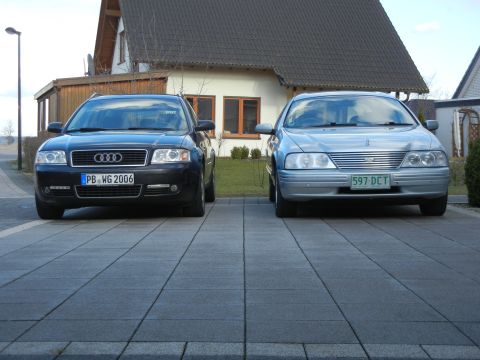 1999 Ford Fairlane - Two sedans are parked side-by-side on a paved driveway in front of a residential building.