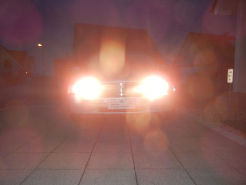 1999 Ford Fairlane - A car's headlights illuminate the scene as it sits parked on a paved surface during twilight.