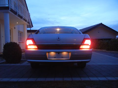 1999 Ford Fairlane - Rear view of a silver sedan at dusk, with its brake lights illuminated and a SUPERMOTORS watermark visible.