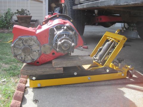 1989 Ford Bronco - A red transfer case is positioned on a yellow jack, resting on wooden blocks.