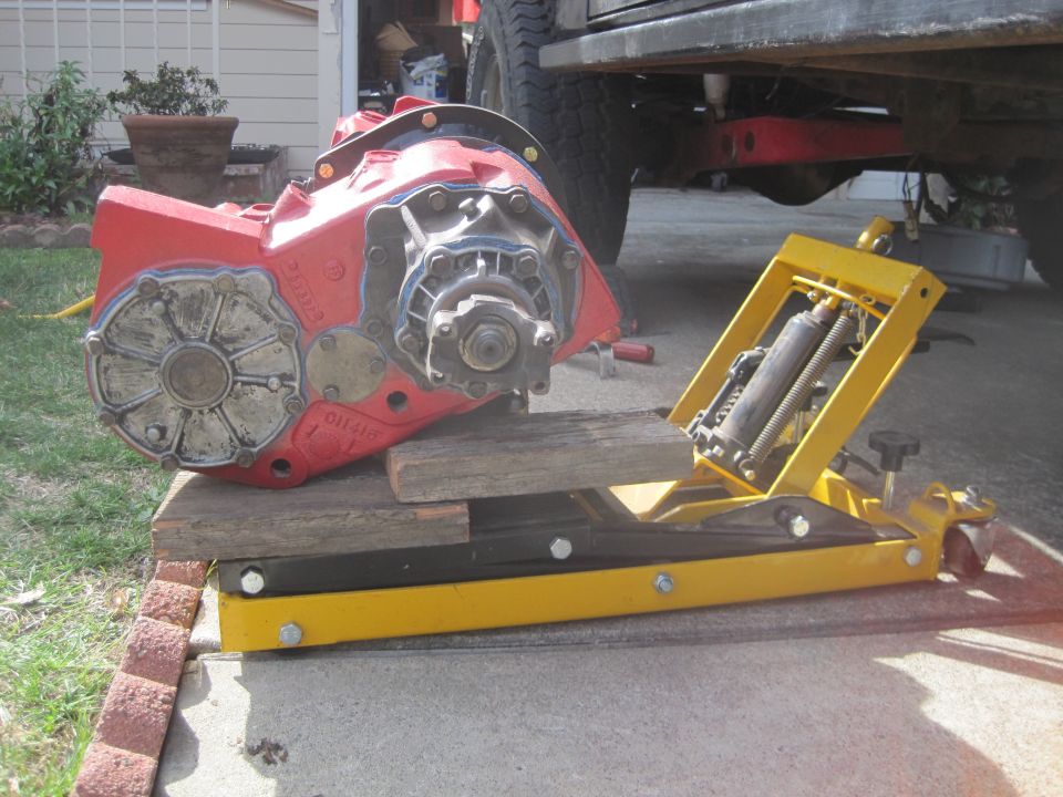 Red transfer case on a yellow hydraulic jack, supported by wood blocks