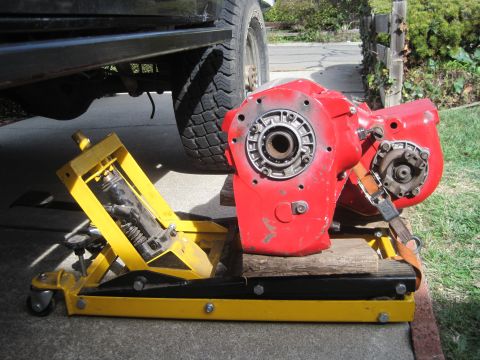 1989 Ford Bronco - A red transfer case assembly is shown mounted on a yellow hydraulic jack, partially underneath a vehicle.