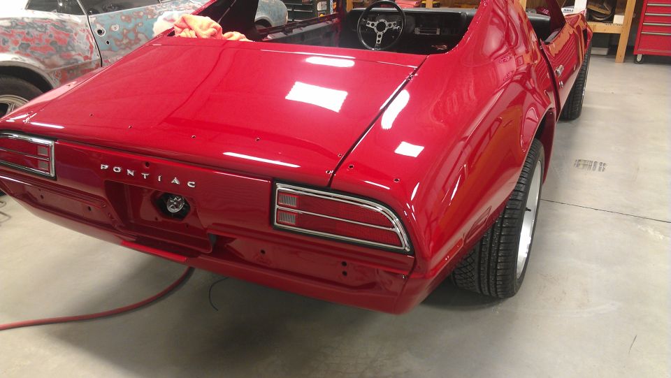 Red Pontiac Firebird undergoing restoration, rear view, showing "PONTIAC" badging and taillights