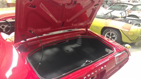 1972 Pontiac Trans Am - The trunk and interior of a red car are shown, with another vehicle in the background. Text on the trunk reads 'PONTIAC'.