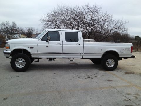 1997 Ford F-350 - A white 1997 Ford F-350 crew cab pickup truck is parked on a paved surface under an overcast sky.
