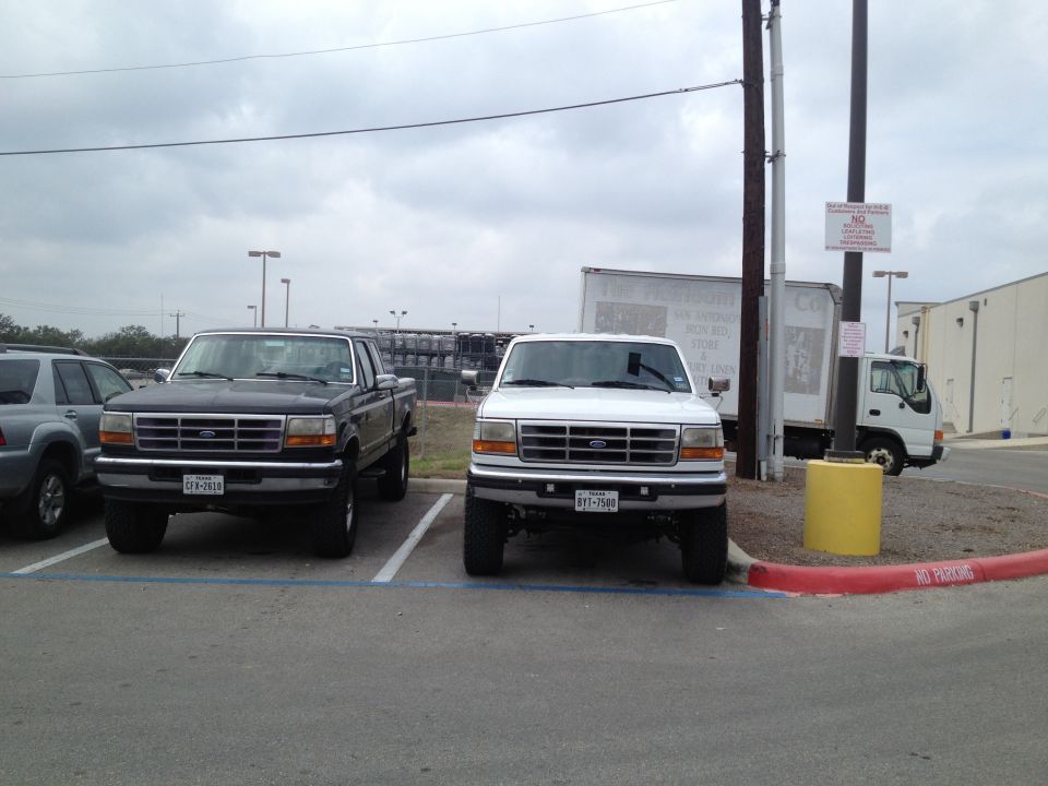 Two 1997 Ford F-350 trucks parked side-by-side, one black and one white, viewed from the front