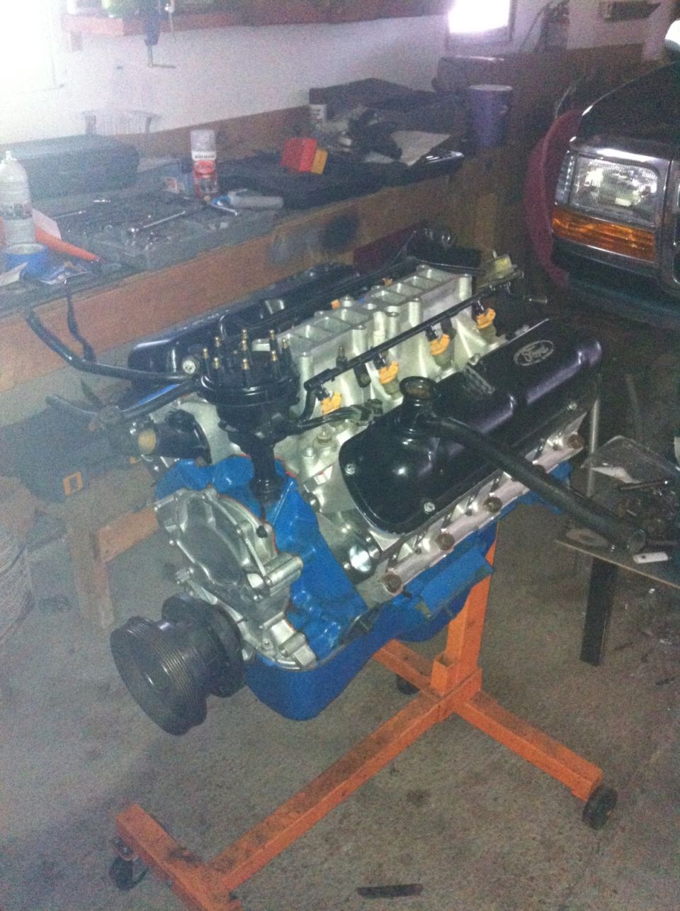 Ford V8 engine on an orange engine stand, with a portion of a dark SUV visible in the background