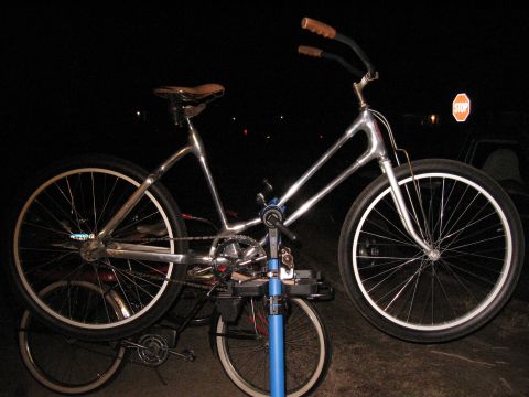 Chrome cruiser bicycle with brown grips and seat, on a repair stand. Another bicycle is visible underneath