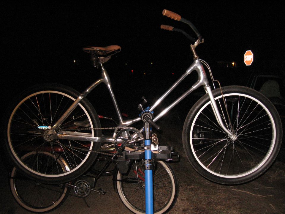 Chrome cruiser bicycle with brown grips and seat, on a repair stand. Another bicycle is visible underneath