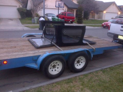 1985 Jeep CJ7 - Disassembled Jeep CJ-series soft top loaded onto a trailer, with residential buildings and vehicles visible.