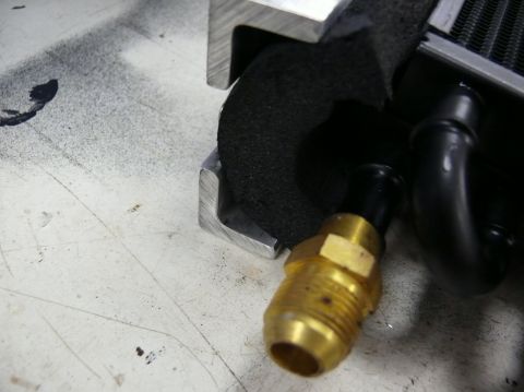 1976 Chevrolet Corvette - Close-up of a brass fitting connected to a black hose and part of a radiator assembly.