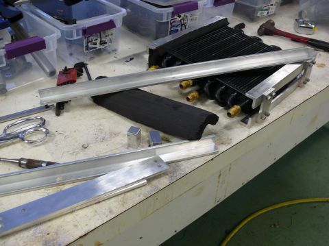 1976 Chevrolet Corvette - Various automotive parts, including an oil cooler and aluminum extrusions, are laid out on a workbench.
