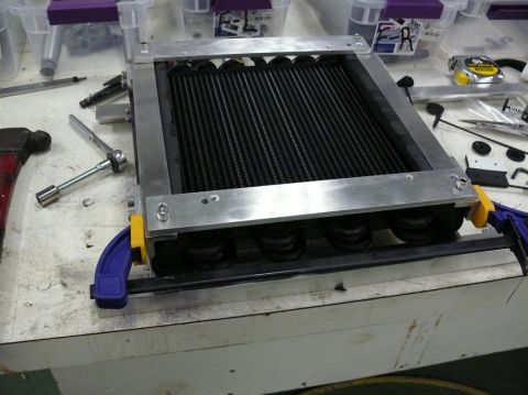 1976 Chevrolet Corvette - A car radiator assembly is clamped to a workbench, surrounded by tools and supplies.