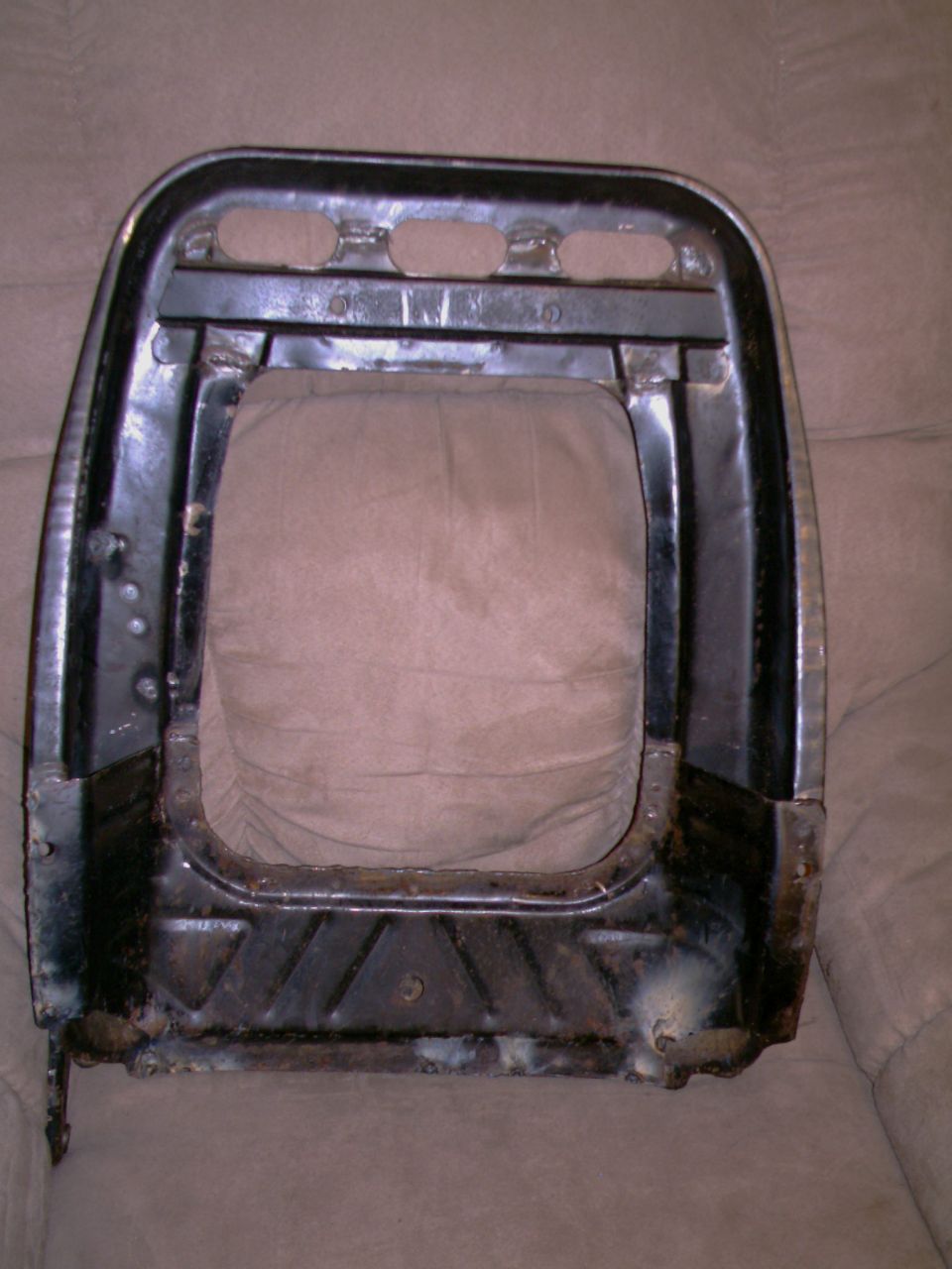 Black metal seat frame with tan fabric backing, showing rust and welds