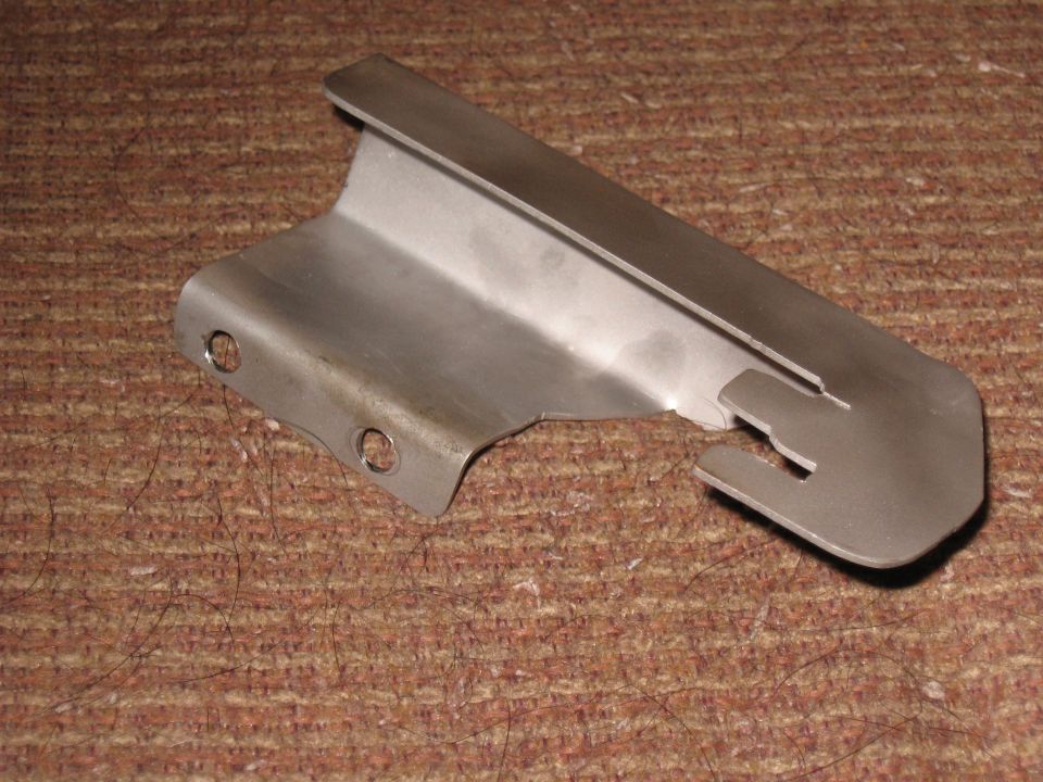 Brushed metal bracket with two mounting holes and a notched end on a brown textured surface.