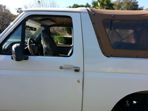 1992 Ford Bronco - This white SUV features a brown soft top and camouflage seat covers, seen from the side.