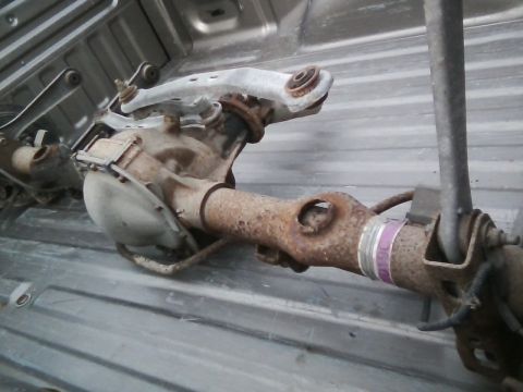 1999 Mercury Grand Marquis - A rusty rear axle assembly and suspension parts are stored in the bed of a pickup truck.