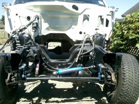 1982 Ford Bronco - The front end of a disassembled 1980s Ford Bronco is shown, revealing its chassis and engine components.