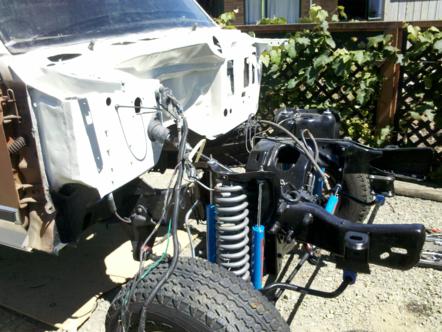 1982 Ford Bronco - The front end of a vehicle is shown with its engine removed, revealing the chassis and suspension system.